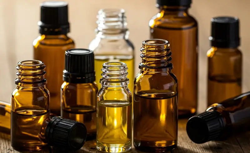 Una colección de aceites esenciales en botellas de color ámbar, sin etiquetas, dispuestos en una mesa de madera.